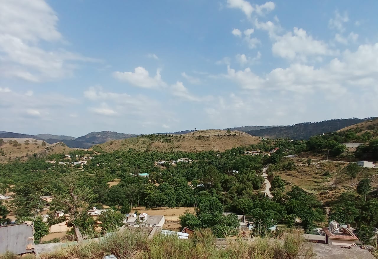 Road access to land for sale in Pir Sohawa Islamabad — road winding through a green valley with village homes